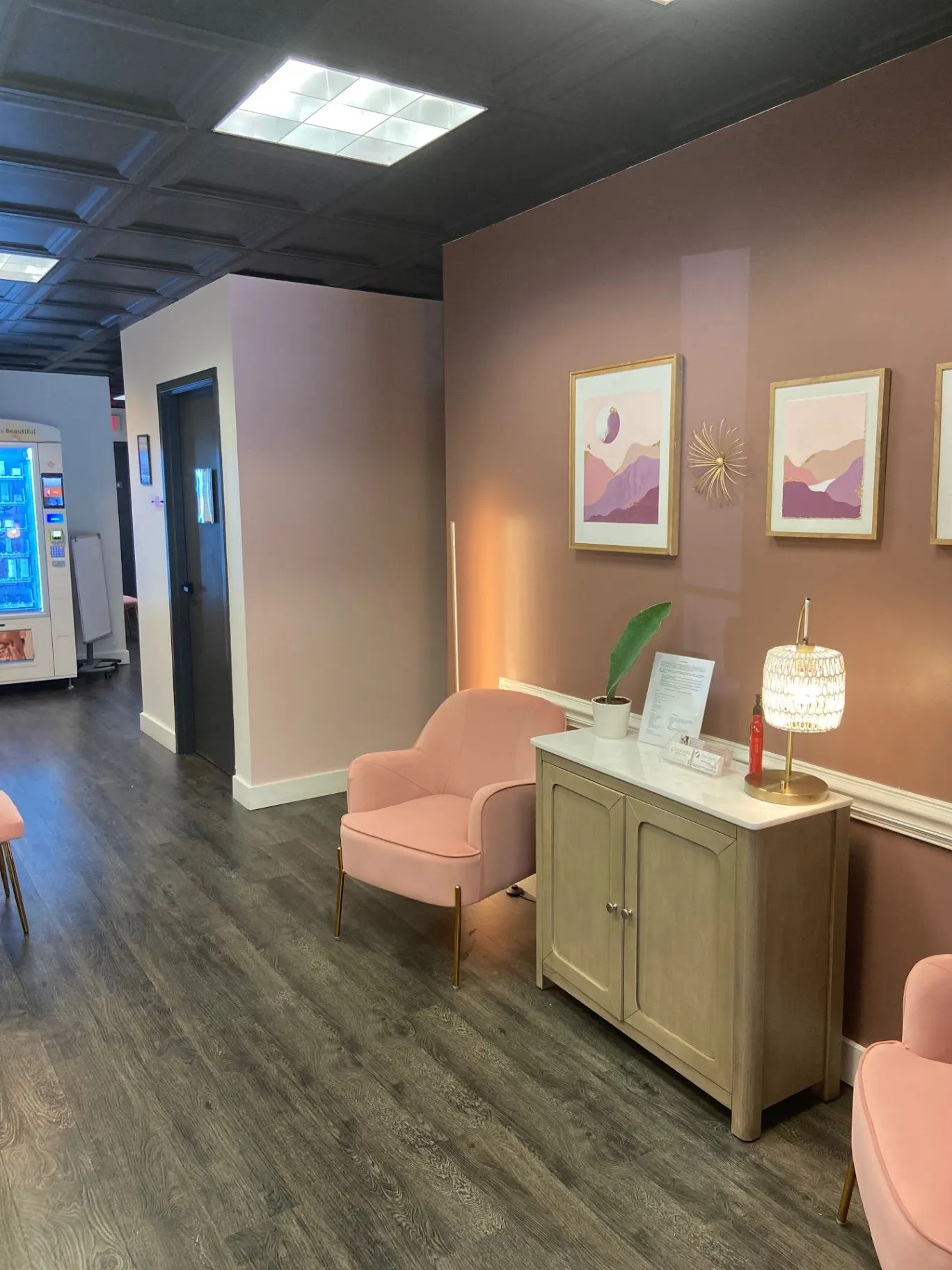 Warm studio reception area with blush chairs, framed art, a cabinet, and a lamp.