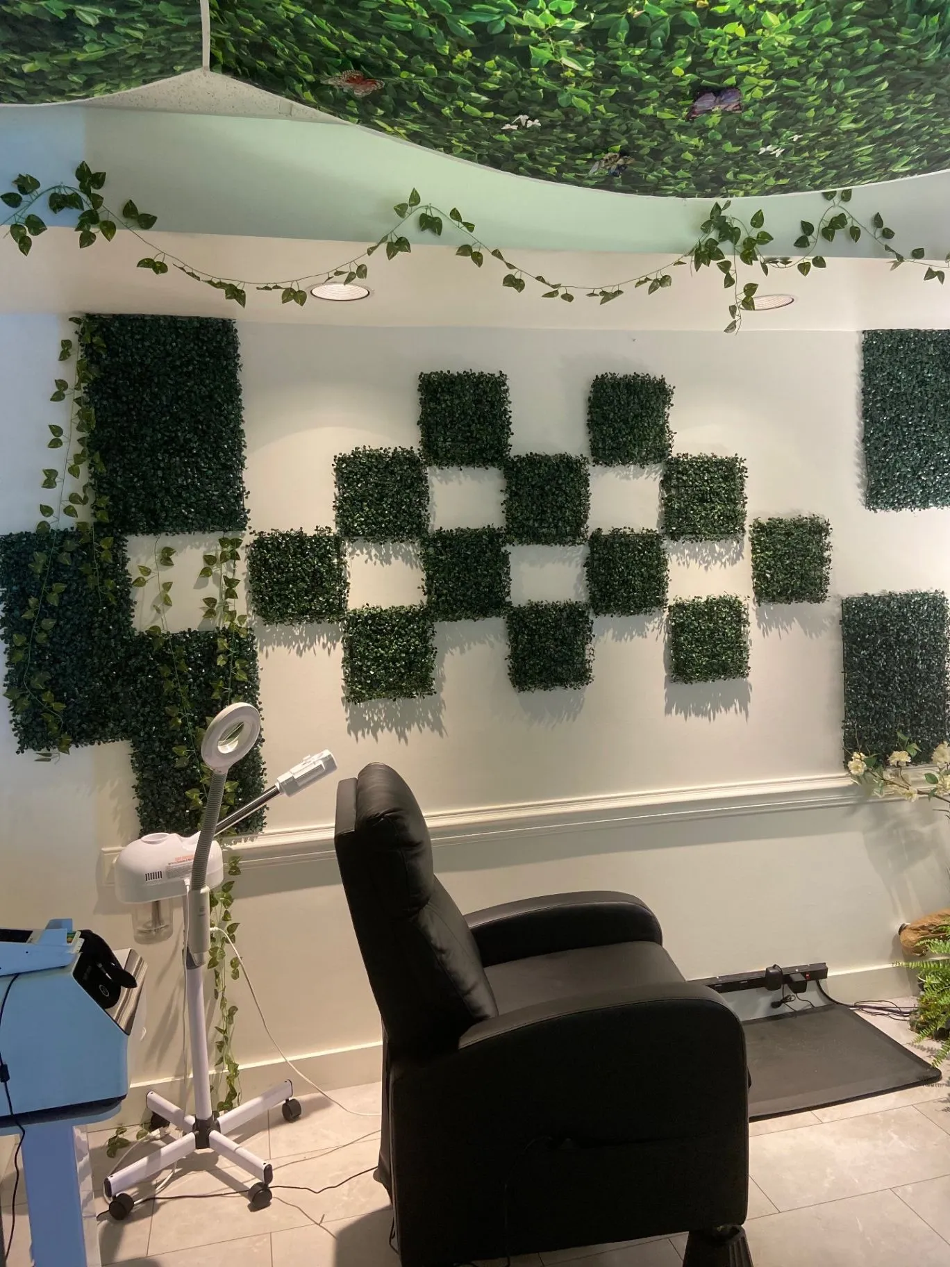 Treatment room with a black chair, greenery-covered wall, and treatment equipment.